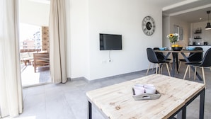 A modern living room with a wooden table, a flat-screen TV mounted on the wall, and a dining area with black chairs and a vase of flowers. - SW Bailen Beautiful views (Málaga)
