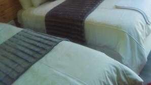 Une chambre d’hôtel avec deux lits, une tête de lit en bois, une fenêtre avec des rideaux et une petite table avec une lampe.
