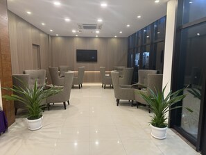A modern waiting area with seating, a flat-screen TV, and potted plants.