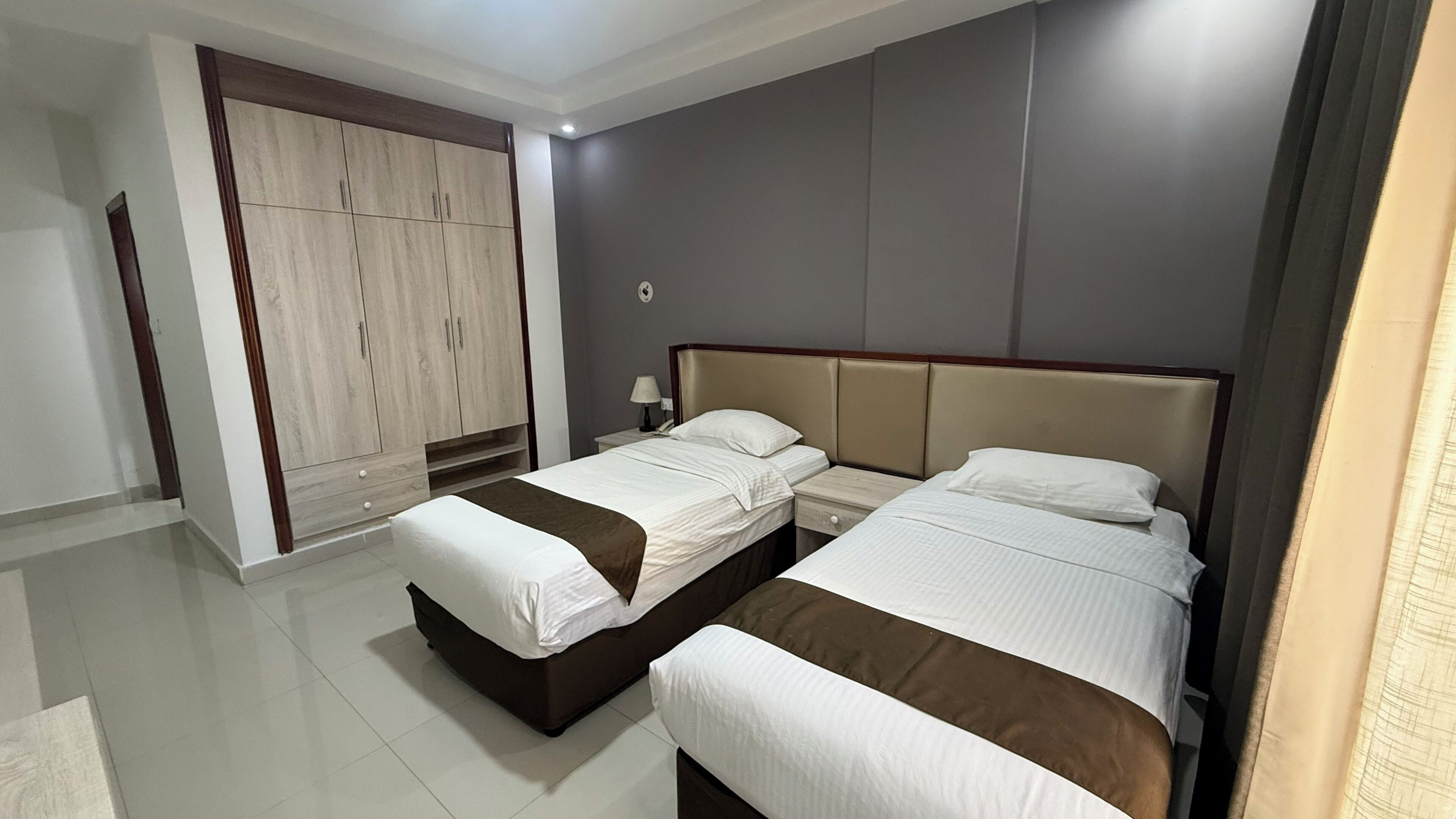 Une chambre d’hôtel avec deux lits, une armoire, une table de chevet et une lampe.