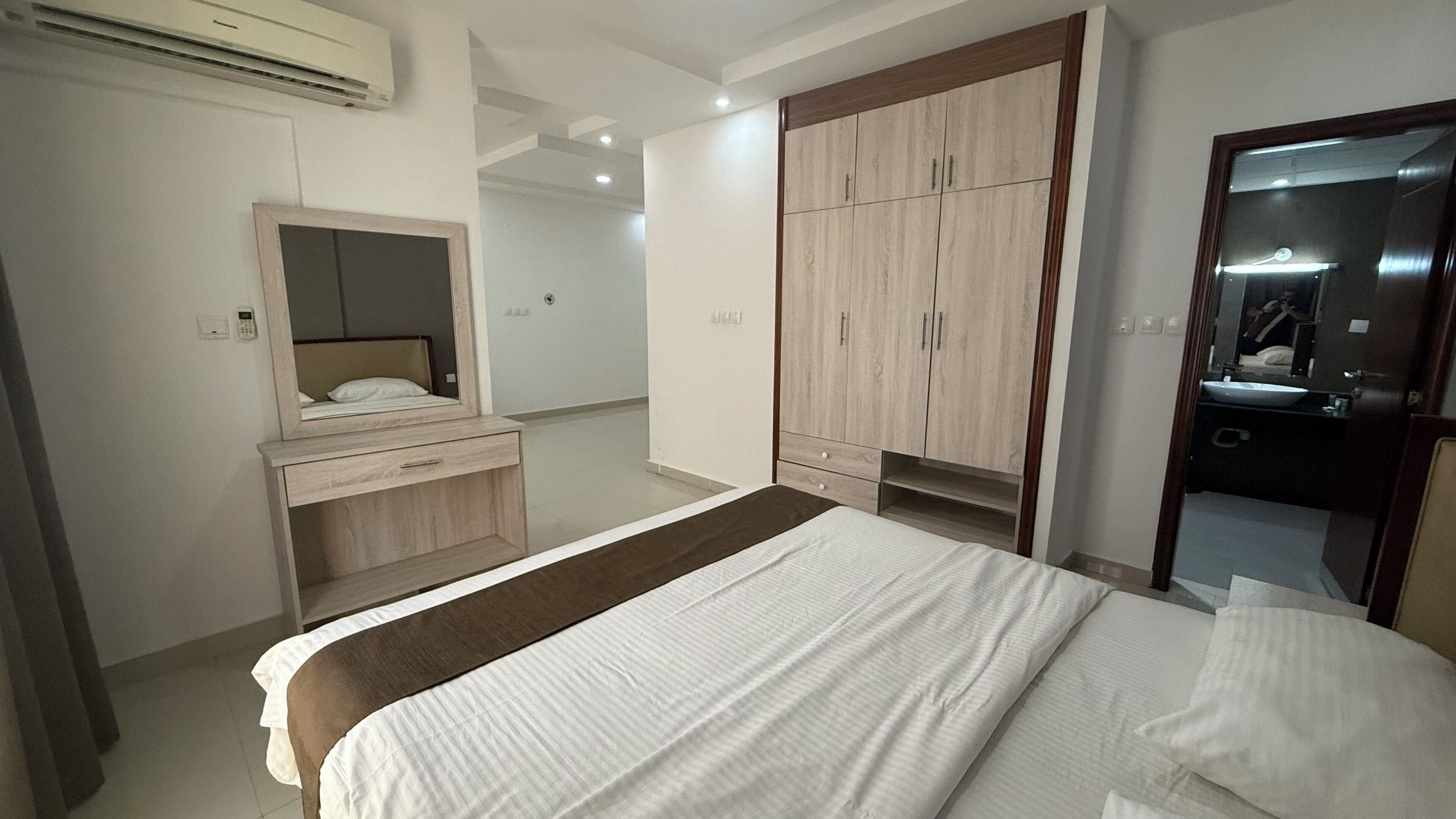 Een hotelkamer met een bed, een kaptafel met spiegel, een kledingkast en een badkamer met wastafel en spiegel.