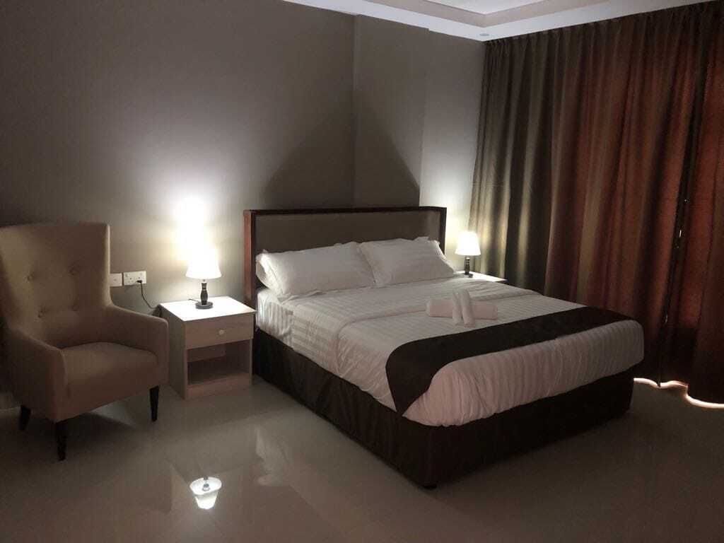 A hotel room with a large bed, two bedside tables with lamps, a chair, and a window with curtains.