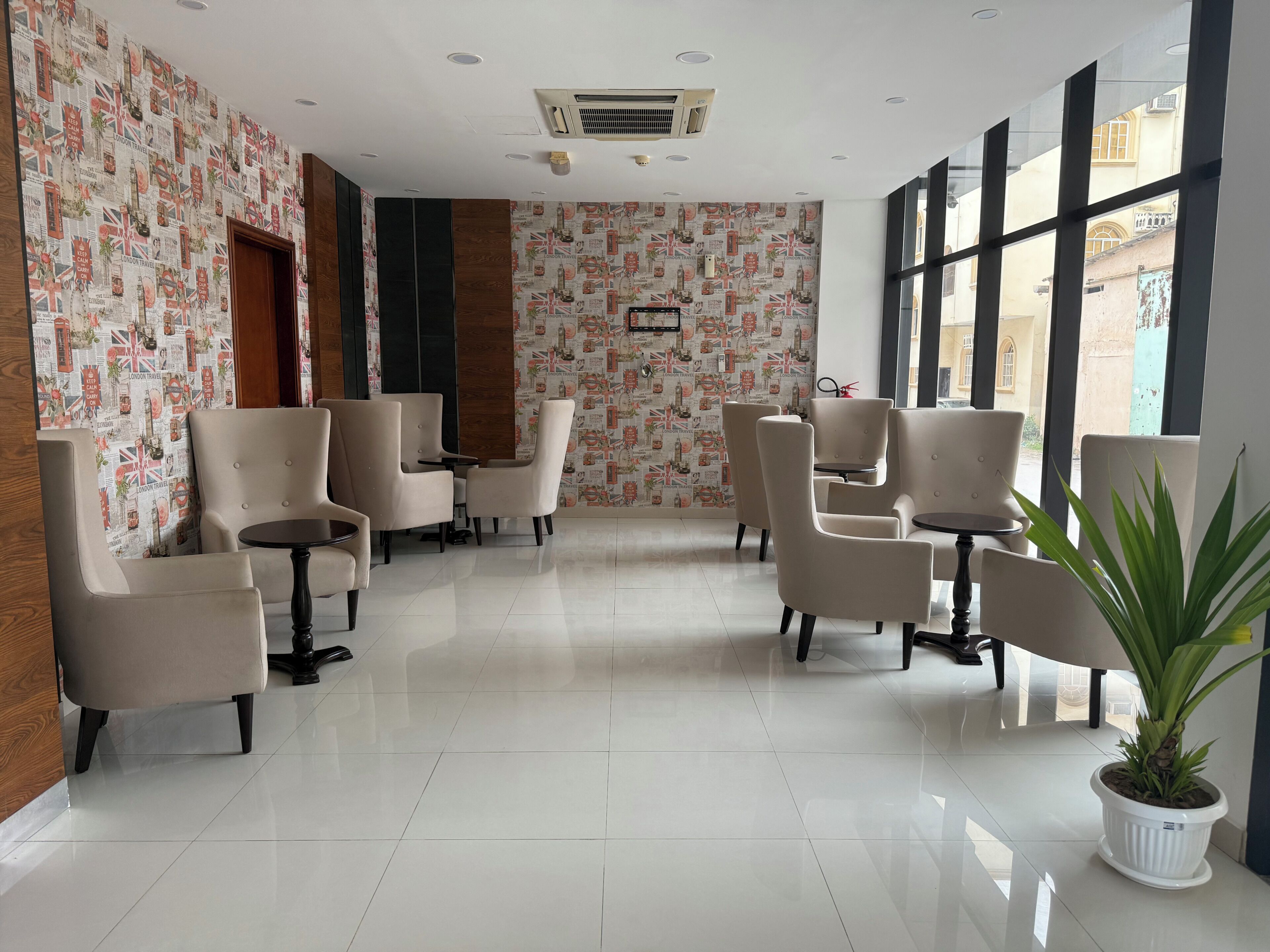 A hotel lobby with a patterned wallpaper, multiple seating areas, and a large window offering a view of the outside.