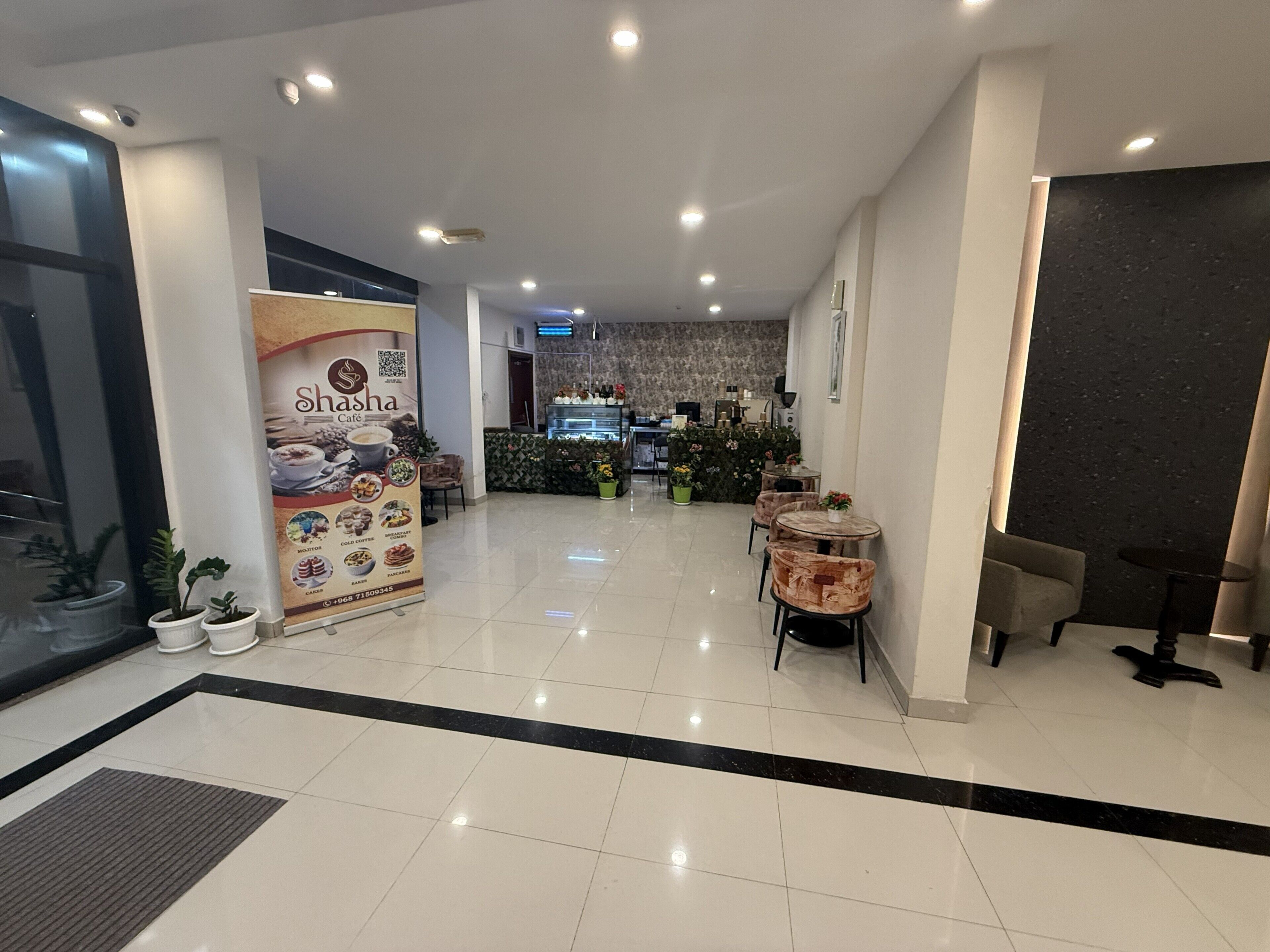 A modern interior with a reception area, a Shasha Café sign, and a seating area with tables and chairs.
