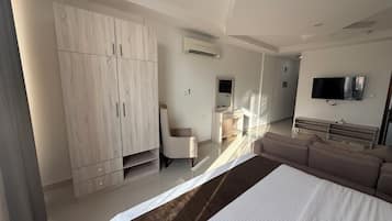 Ein modernes Hotelzimmer mit großem Kleiderschrank, Schreibtisch mit Spiegel, einer Couch und einem wandmontierten Flachbildfernseher.