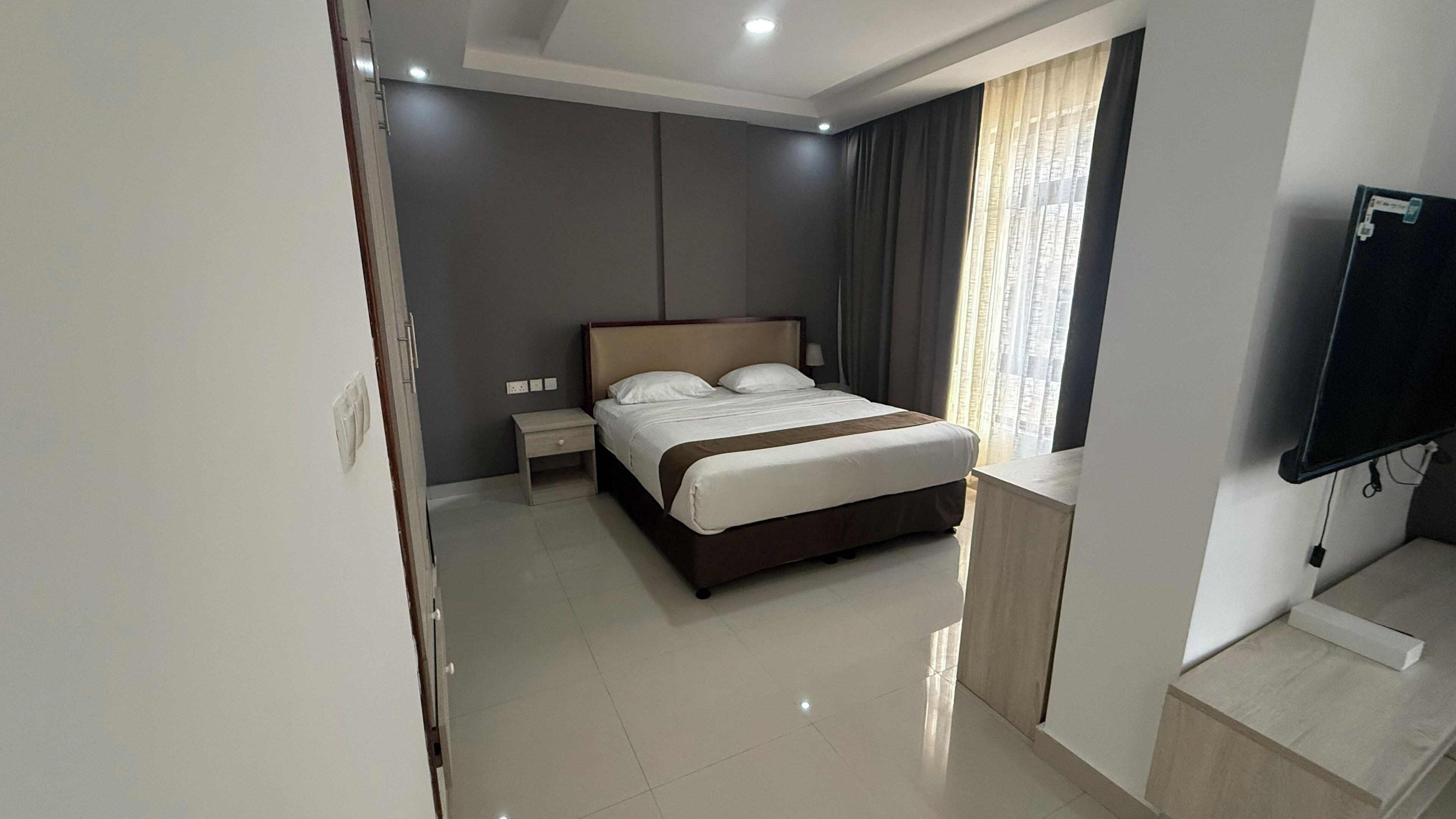 A modern hotel room with a bed, bedside table, and a flat-screen TV mounted on the wall.