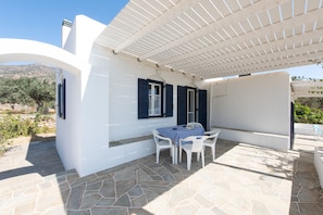 Un edificio blanco con contraventanas azules, un patio de piedra y una zona de estar al aire libre cubierta.
