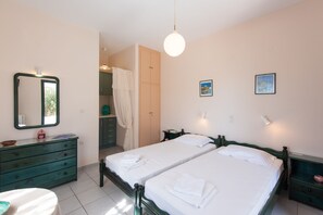 A bedroom with two beds, a dresser, a mirror, and a hanging light fixture. - Elisso Villas (Sifnos)