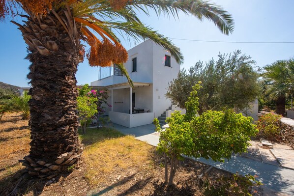 A modern two-story house with a flat roof, a balcony, and a stone base. - Elisso Villas (Sifnos)