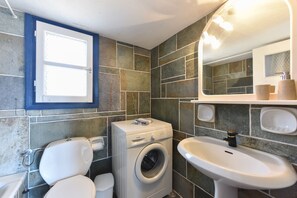A compact bathroom with a washing machine, toilet, and sink. - Elisso Villas (Sifnos)