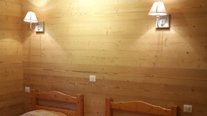 Ein Zimmer mit zwei Holzbetten, jeweils mit Kopfteil und kleinem Nachttisch. An jeder Seite der Betten befinden sich Wandleuchten.