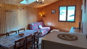 Ein gemütliches Blockhaus mit Holzausstattung, einem Esstisch mit Stühlen, einer Couch und einem kleinen Tisch mit Lampe.