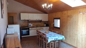 Eine kompakte Küche mit Holzschränken, einem Esstisch mit Stühlen, einer Deckenleuchte und einem Fenster.