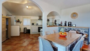 Une cuisine spacieuse avec un coin repas, agrémentée d’un mur en pierre, d’une table en bois et d’un panier de fruits.