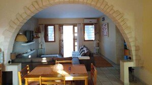 A dining area with a table and chairs, a sofa, and a kitchen area with a stove and shelves.