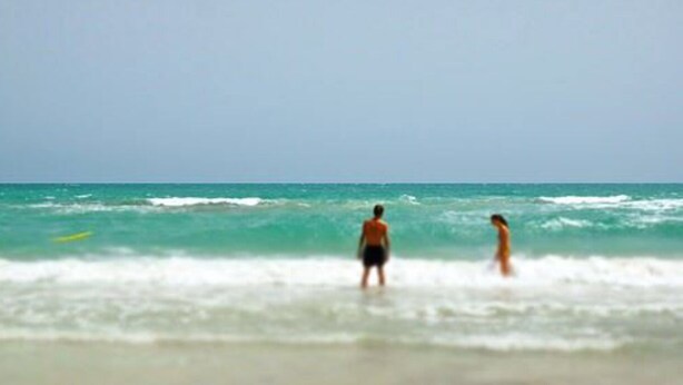 A beach scene with two people in the water.