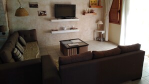 A living room with a sofa, a coffee table, a TV on a shelf, and a lamp.