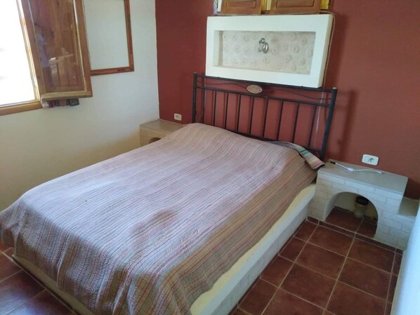 Une chambre à coucher comprenant un lit, une table de chevet, une petite armoire et un sol carrelé.