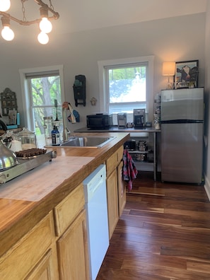 Una cocina con armarios de madera, lavavajillas, refrigerador, cafetera y ventana con vista a árboles.