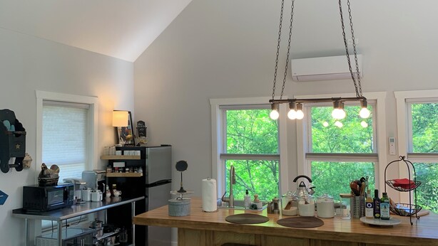 Une cuisine moderne avec un îlot central en bois, des tabourets de bar, un ventilateur de plafond et de grandes fenêtres donnant sur un paysage verdoyant.