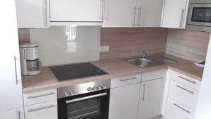A modern kitchen with white cabinets, a stainless steel sink, a built-in oven, and a coffee maker.