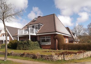 Une maison à deux étages avec un balcon, une façade en briques et un mur en pierre à l’avant.