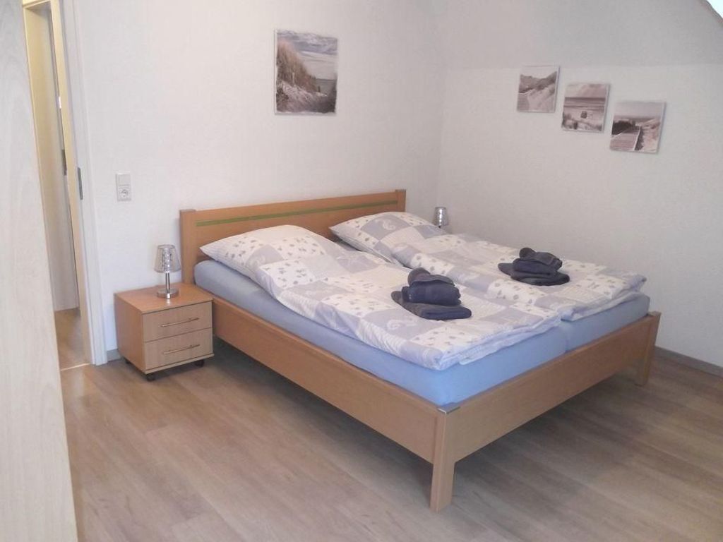 Ein Doppelbett mit Holzrahmen, ein Nachttisch mit Schubladen und ein Beistelltisch mit Lampe.
