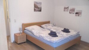 A double bed with a wooden frame, a nightstand with drawers, and a bedside table with a lamp.