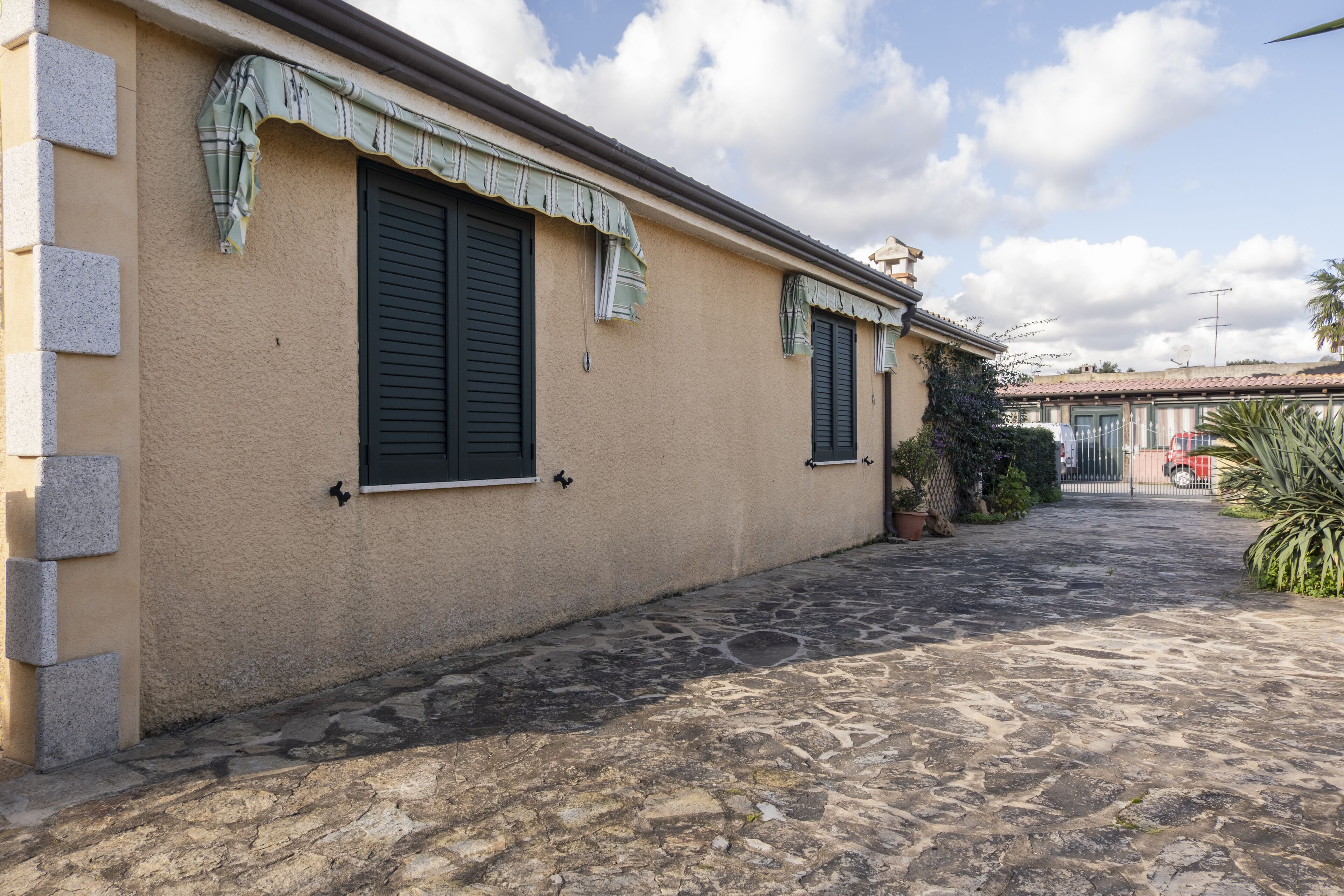 A building with a stone-paved courtyard, two windows with shutters, and a gated entrance.
