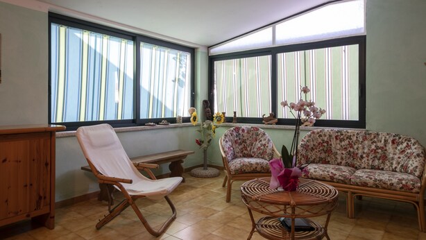 A room with a wooden bench, a white chair, a floral sofa, and a wicker table. - Aria di Vacanza - Maltineddu COD 23 (Olbia)