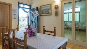 A dining area with a table set for four, wooden chairs, a vase with flowers, and a painting on the wall. - Aria di Vacanza - Maltineddu COD 23 (Olbia)
