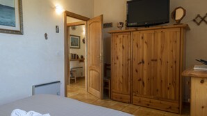 A bedroom with a bed, a wooden wardrobe, a television, and a small table. - Aria di Vacanza - Maltineddu COD 23 (Olbia)
