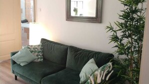 Olohuoneessa on vihreä sohva, pyöreä sohvapöytä, jonka päällä on kasvi, ja seinällä on peili.