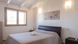 A bedroom with a bed, a nightstand, a dresser, a window, and a wall-mounted light fixture.