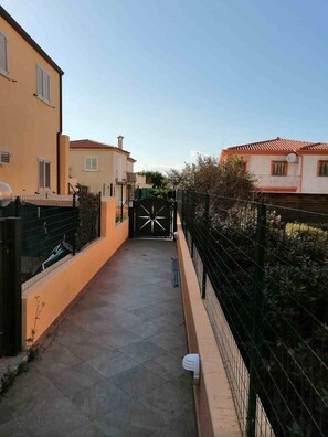 A narrow pathway leading to a gated entrance with a gate that has a tricycle symbol. - Aria di Vacanza - Sìabba Lughente Primo COD 17 (Olbia)