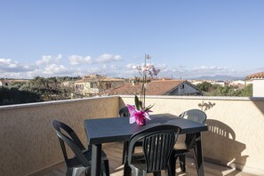 A balcony with a table and chairs, a potted orchid, and a view of a town with buildings and mountains in the distance. - Aria di Vacanza - Sìabba Lughente Primo COD 17 (Olbia)