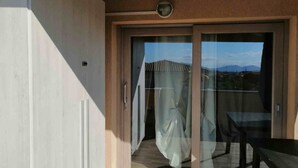 A balcony with a sliding glass door, a table, and a view of a mountainous landscape.