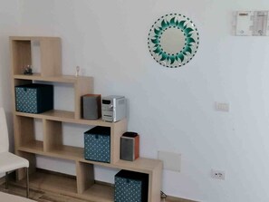 A room with a wooden shelving unit containing various items, a decorative mirror, and a power outlet on the wall. - Aria di Vacanza - Sìabba Lughente Primo COD 17 (Olbia)