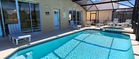 A covered outdoor swimming pool with lounge chairs and a glass door entrance.