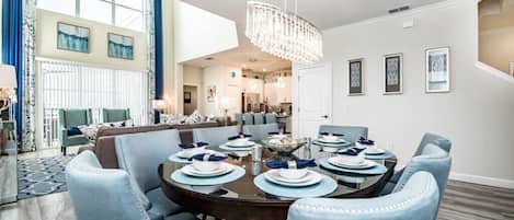A dining area with a round table set for six, surrounded by six blue upholstered chairs.