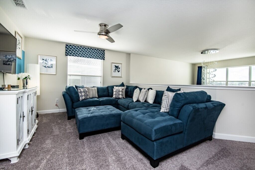 A modern living room with a sectional sofa, a ceiling fan, and a large window with blinds.