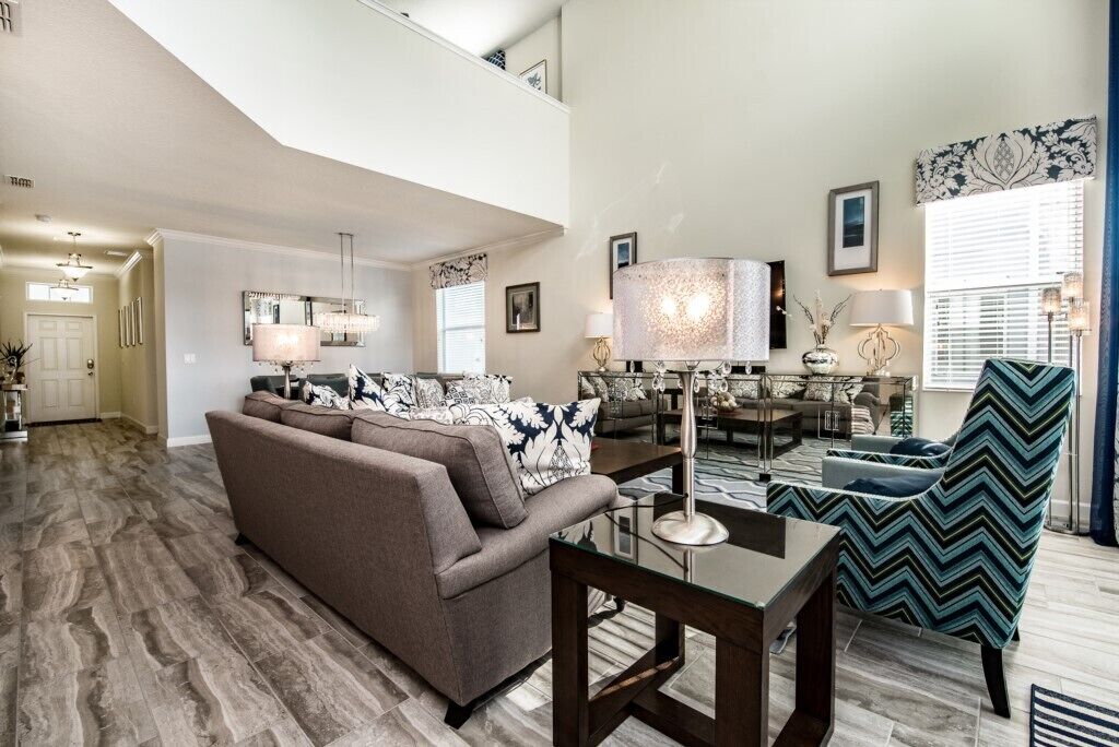 A spacious living room with a brown sofa, a glass coffee table, and a patterned armchair.