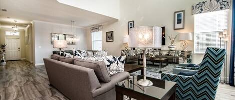 A spacious living room with a brown sofa, a glass coffee table, and a patterned armchair.