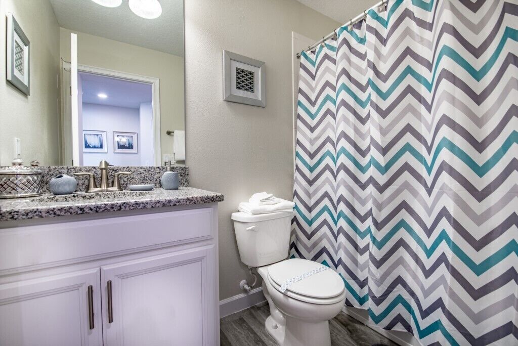 Une salle de bain avec des toilettes blanches, un rideau de douche à motifs en zigzag et un meuble-lavabo avec un plan de travail en marbre.