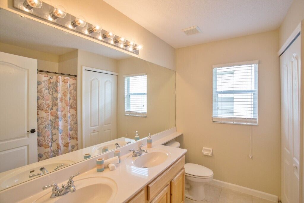 A bathroom with a double sink vanity, a large mirror, and a toilet.