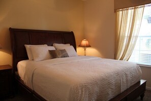 A neatly made bed with a white quilt, a wooden headboard, and a bedside lamp.