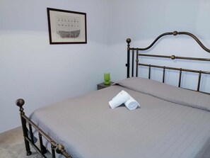 Un lit simple avec un cadre en métal, une table de chevet verte et un tableau encadré accroché au mur.