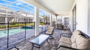 A covered outdoor area with a pool, lounge chairs, and a glass-enclosed patio. - 1669MVD Amazing Champions Gate 8 Bedroom 5 Bed Villa by RedAwning (Davenport)