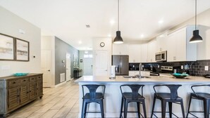 A modern kitchen with white cabinets, a central island with bar stools, and stainless steel appliances. - 1669MVD Amazing Champions Gate 8 Bedroom 5 Bed Villa by RedAwning (Davenport)