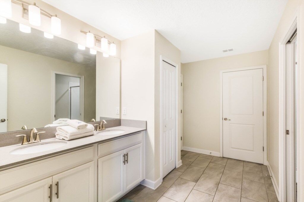 A bathroom with a double sink vanity, a large mirror, and a walk-in shower.